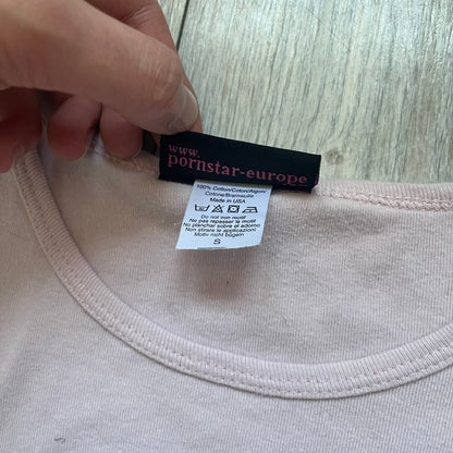 Pornstar Clothing My Little Pony Pink Tee is a women’s baby pink T-shirt featuring a front graphic of two My Little Pony characters under a “My Little Porny” text on a rainbow. A small Pornstar logo sits below the graphic, and the neck tag is black and pink with Pornstar branding. Super rare and hard to find piece.