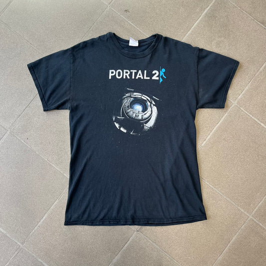 Portal 2: Wheatley in Space 2011 J!nx Tee features a black T-shirt made on a Gildan blank by J!NX in collaboration with Valve. The front has a graphic of Wheatley floating in space with a white and blue Portal 2 logo above him. Made from 100% cotton.
