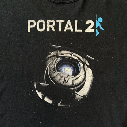 Portal 2: Wheatley in Space 2011 J!nx Tee features a black T-shirt made on a Gildan blank by J!NX in collaboration with Valve. The front has a graphic of Wheatley floating in space with a white and blue Portal 2 logo above him. Made from 100% cotton.
