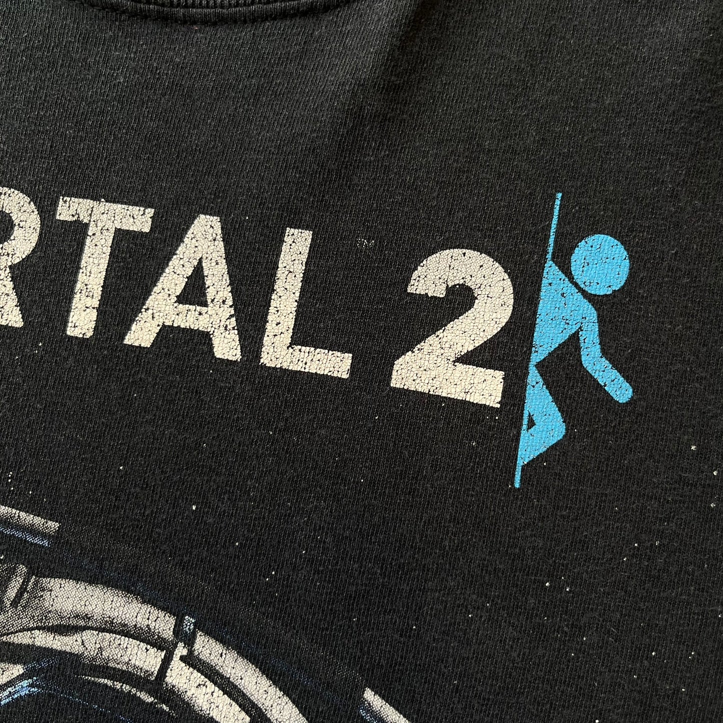 Portal 2: Wheatley in Space 2011 J!nx Tee features a black T-shirt made on a Gildan blank by J!NX in collaboration with Valve. The front has a graphic of Wheatley floating in space with a white and blue Portal 2 logo above him. Made from 100% cotton.

