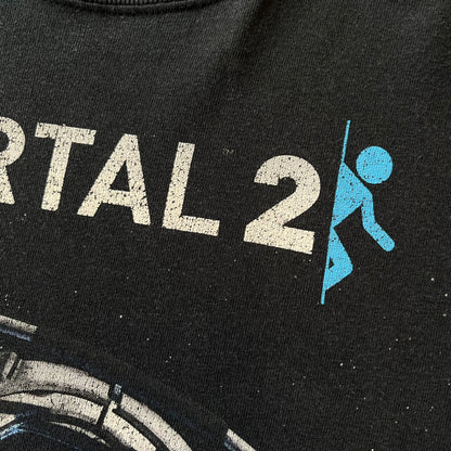 Portal 2: Wheatley in Space 2011 J!nx Tee features a black T-shirt made on a Gildan blank by J!NX in collaboration with Valve. The front has a graphic of Wheatley floating in space with a white and blue Portal 2 logo above him. Made from 100% cotton.
