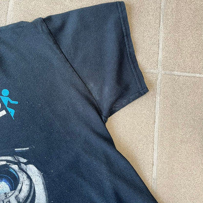 Portal 2: Wheatley in Space 2011 J!nx Tee features a black T-shirt made on a Gildan blank by J!NX in collaboration with Valve. The front has a graphic of Wheatley floating in space with a white and blue Portal 2 logo above him. Made from 100% cotton.
