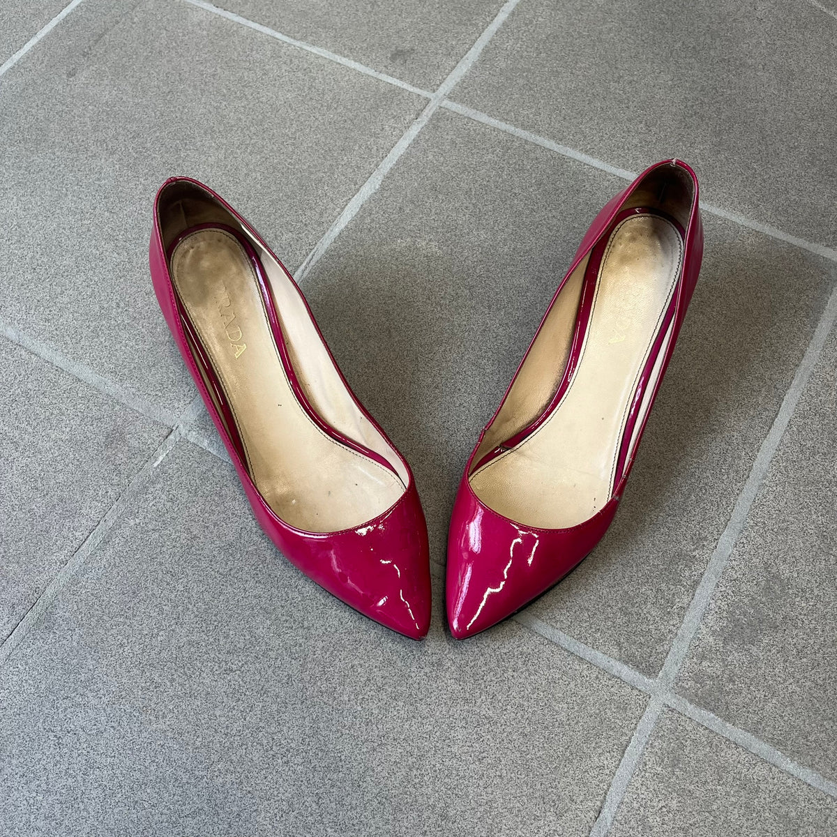 Prada 2000's Patent Leather Magenta Kitten Heels are made in Italy from magenta patent leather with a beige interior and sole, featuring a gold-tone metal Prada logo on the bottom and Prada branding on the insole. They come with the original box and two dust bags; the bottom and heel tip have been professionally repaired.