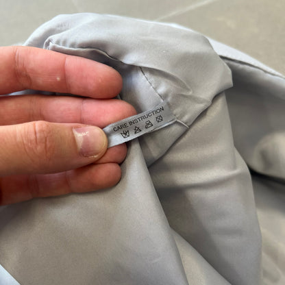 Prada 2012 Luna Rossa Drawstring Sling Bag is a light gray, almost silvery sling bag made as a gift-with-purchase for the Luna Rossa fragrance. It features a red rubber stripe at the bottom with white "Prada" and "Luna Rossa" text, and Prada branding on the drawstring toggle.