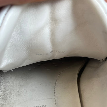 Prada Brushed Leather 2022 White Sneakers feature a classic low-top silhouette crafted from smooth white brushed leather. The outer sides are detailed with Prada's iconic enamel triangle logo plaques in white and silver-tone metal. Made in Italy.
