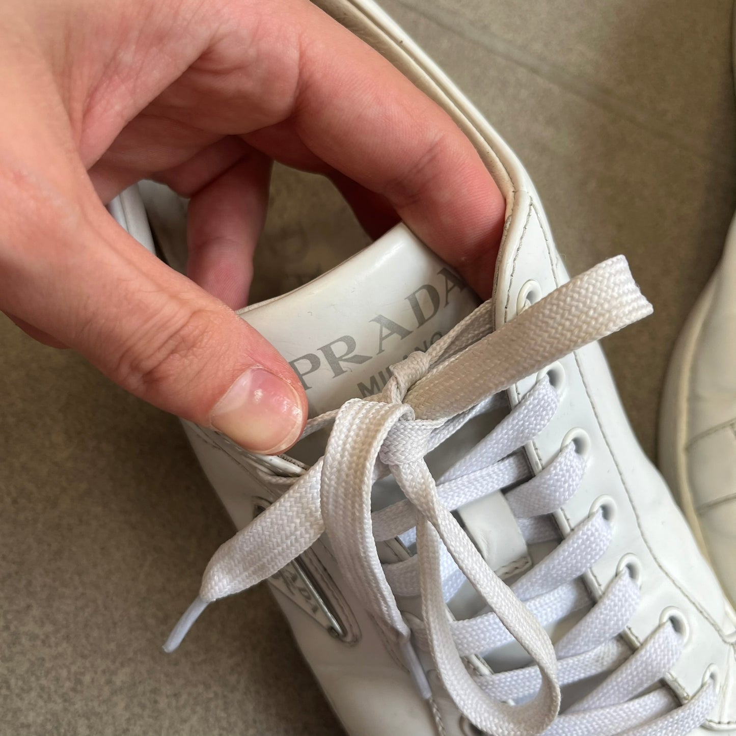 Prada Brushed Leather 2022 White Sneakers feature a classic low-top silhouette crafted from smooth white brushed leather. The outer sides are detailed with Prada's iconic enamel triangle logo plaques in white and silver-tone metal. Made in Italy.