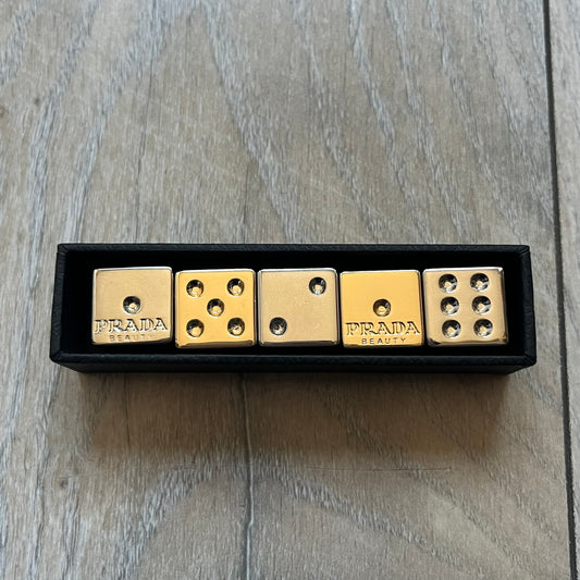 Prada Gold and Silver Dice Set consisting of five metal dice, including two gold-tone and three silver-tone pieces (color finish, not solid gold or silver). Each die is fully metal and has the Prada logo engraved on the face with the number one. The set was released in limited quantities as a promotional addition to Prada fragrances and comes with a Prada Beauty paper box