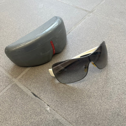 Prada Linea Rossa SPS57G White Sunglasses are shield-style sunglasses featuring a single dark wraparound lens and white arms. One temple is finished with the signature red Prada Linea Rossa logo insert, while the nose pads feature subtle Prada branding. Made in Italy, the sunglasses are lightweight sporty design&nbsp;and they come complete with the original Prada case.
