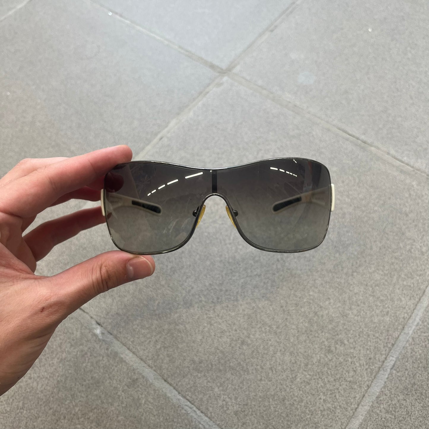 Prada Linea Rossa SPS57G White Sunglasses are shield-style sunglasses featuring a single dark wraparound lens and white arms. One temple is finished with the signature red Prada Linea Rossa logo insert, while the nose pads feature subtle Prada branding. Made in Italy, the sunglasses are lightweight sporty design&nbsp;and they come complete with the original Prada case.