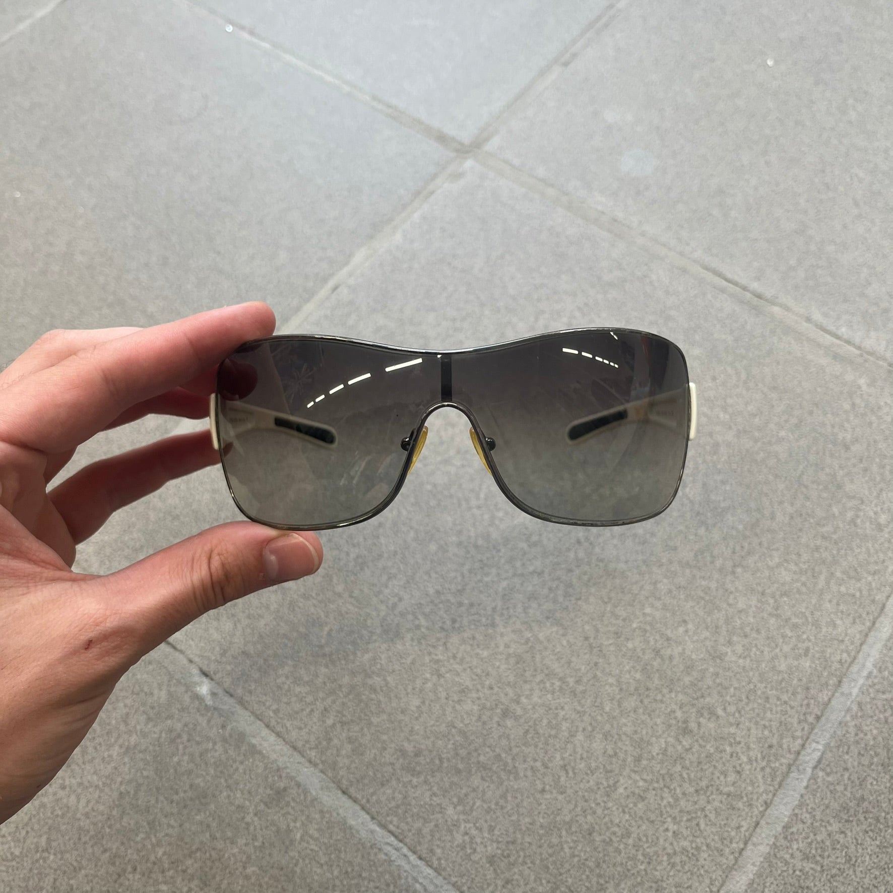 Prada Linea Rossa SPS57G White Sunglasses are shield-style sunglasses featuring a single dark wraparound lens and white arms. One temple is finished with the signature red Prada Linea Rossa logo insert, while the nose pads feature subtle Prada branding. Made in Italy, the sunglasses are lightweight sporty design&nbsp;and they come complete with the original Prada case.