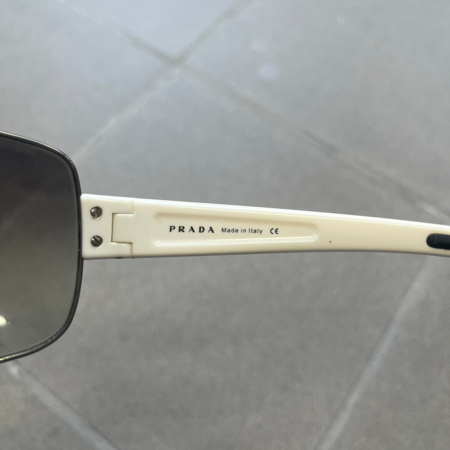 Prada Linea Rossa SPS57G White Sunglasses are shield-style sunglasses featuring a single dark wraparound lens and white arms. One temple is finished with the signature red Prada Linea Rossa logo insert, while the nose pads feature subtle Prada branding. Made in Italy, the sunglasses are lightweight sporty design&nbsp;and they come complete with the original Prada case.