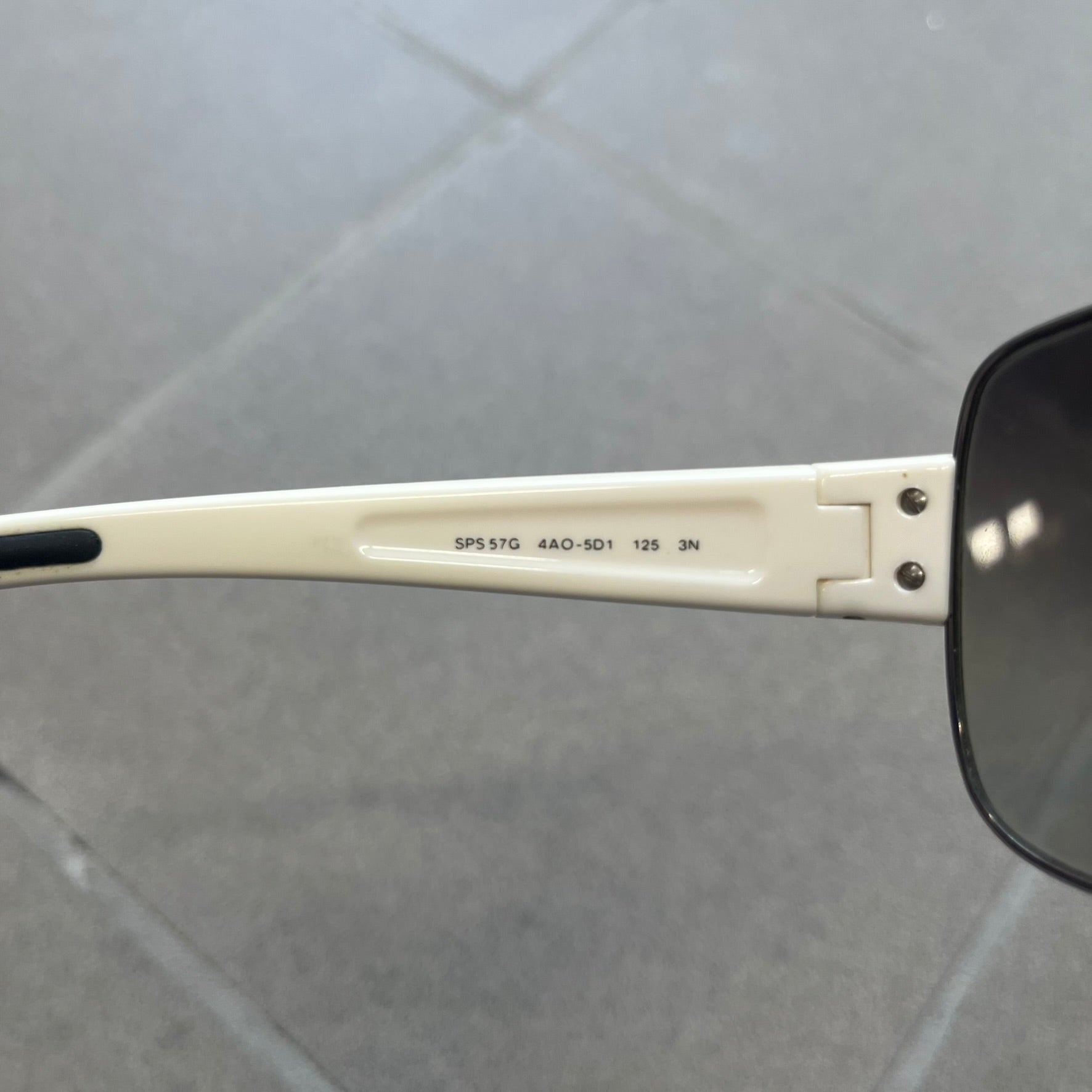 Prada Linea Rossa SPS57G White Sunglasses are shield-style sunglasses featuring a single dark wraparound lens and white arms. One temple is finished with the signature red Prada Linea Rossa logo insert, while the nose pads feature subtle Prada branding. Made in Italy, the sunglasses are lightweight sporty design&nbsp;and they come complete with the original Prada case.