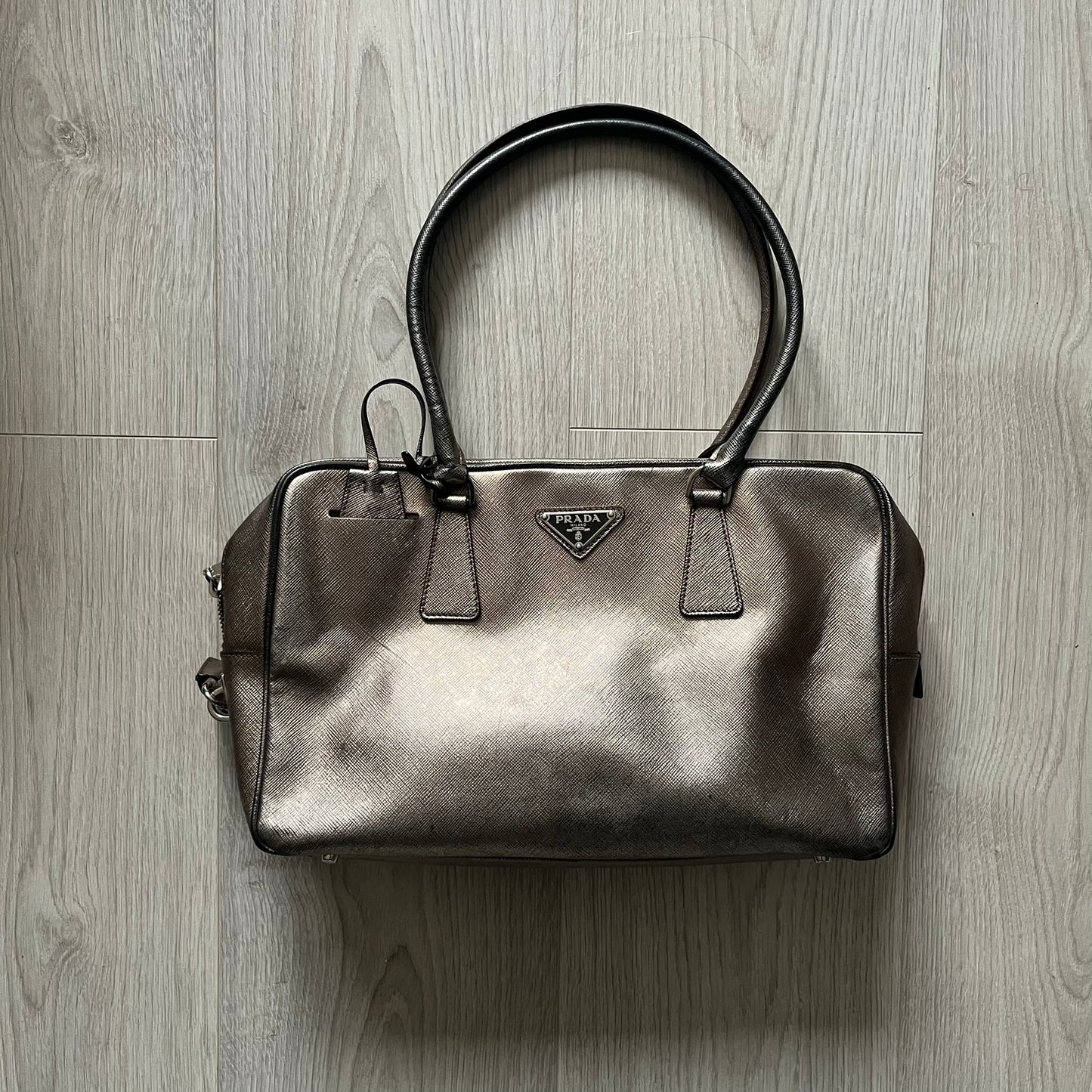 Vintage Prada Metallic Saffiano Bauletto Bag crafted from metallic gold saffiano leather embodies vintage elegance and modern luxury. Detailed with gold-tone hardware, dual handles, and original accessories, it’s a testament to Prada’s enduring craftsmanship. A collector’s piece made to shine on any occasion.