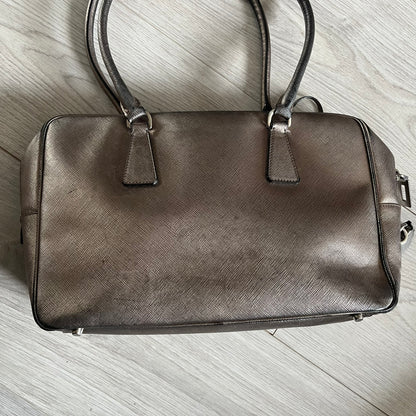 Vintage Prada Metallic Saffiano Bauletto Bag crafted from metallic gold saffiano leather embodies vintage elegance and modern luxury. Detailed with gold-tone hardware, dual handles, and original accessories, it’s a testament to Prada’s enduring craftsmanship. A collector’s piece made to shine on any occasion.
