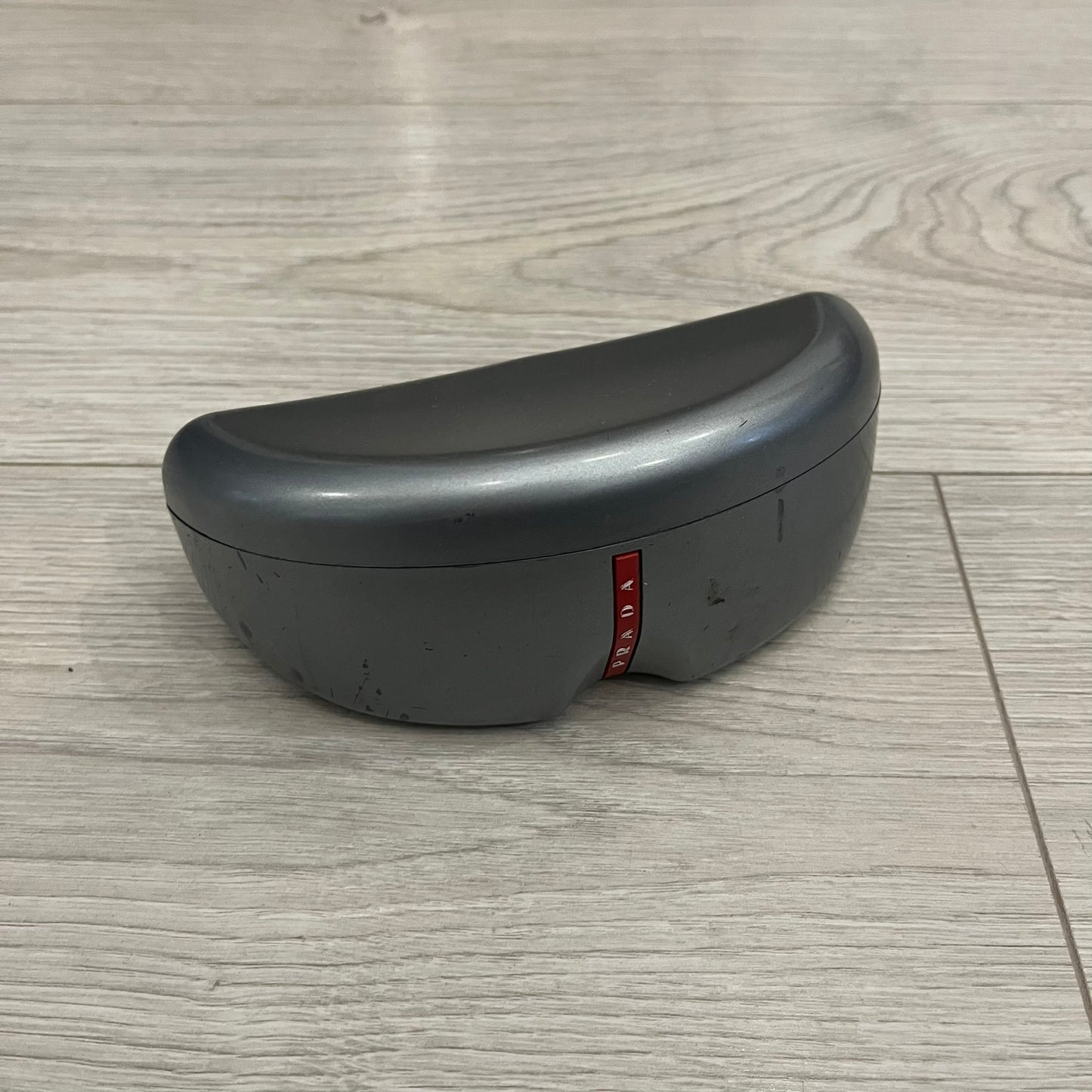 Prada SPS 53H Black/Silver Sunglasses are a vintage wraparound pair featuring a black frame with gunmetal silver accents. The gray lenses are complemented by red details on the arms and visible screws on the front, with Prada branding on the temples. Crafted in Italy from metal and resin, they come complete with the original Prada case.