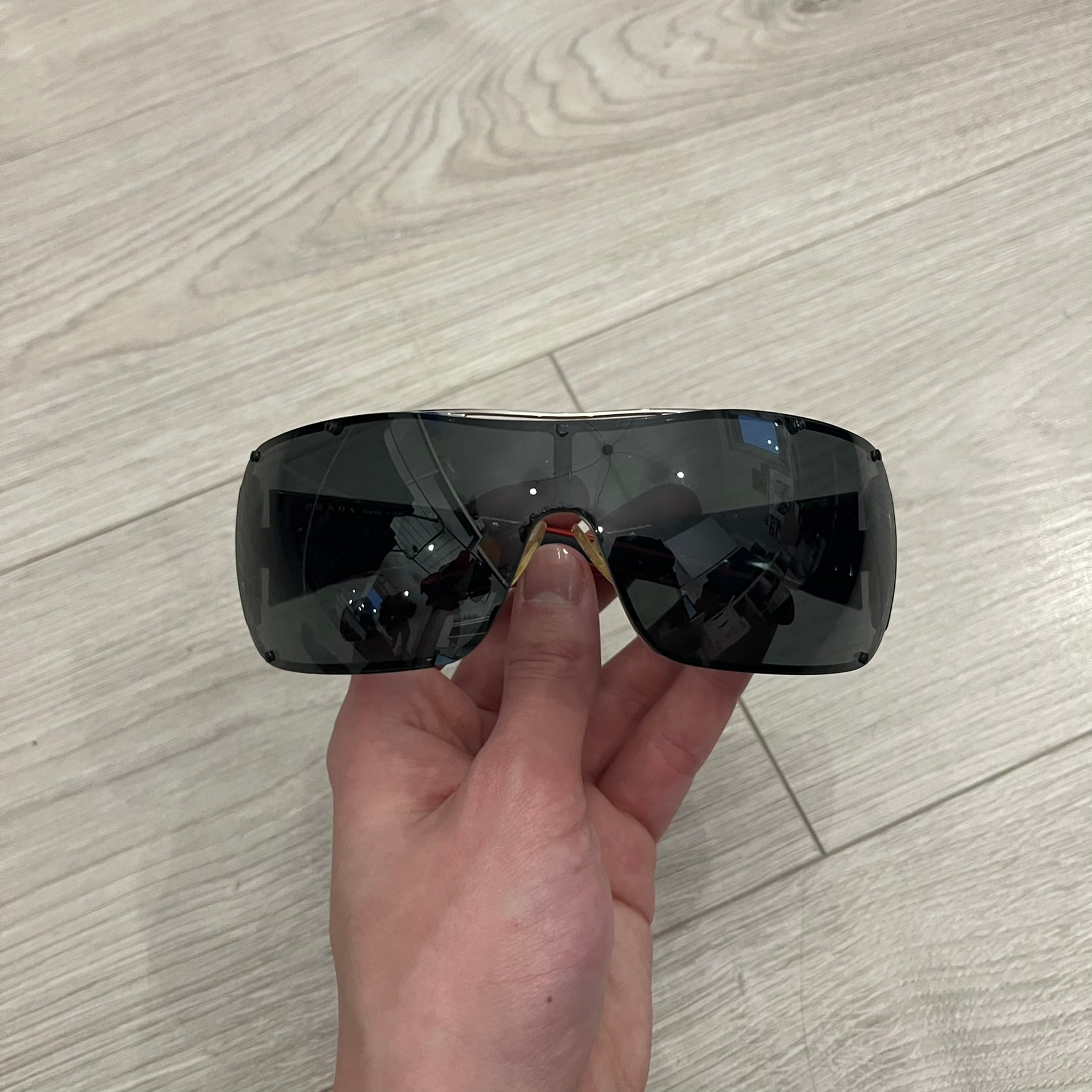 Prada SPS 53H Black/Silver Sunglasses are a vintage wraparound pair featuring a black frame with gunmetal silver accents. The gray lenses are complemented by red details on the arms and visible screws on the front, with Prada branding on the temples. Crafted in Italy from metal and resin, they come complete with the original Prada case.