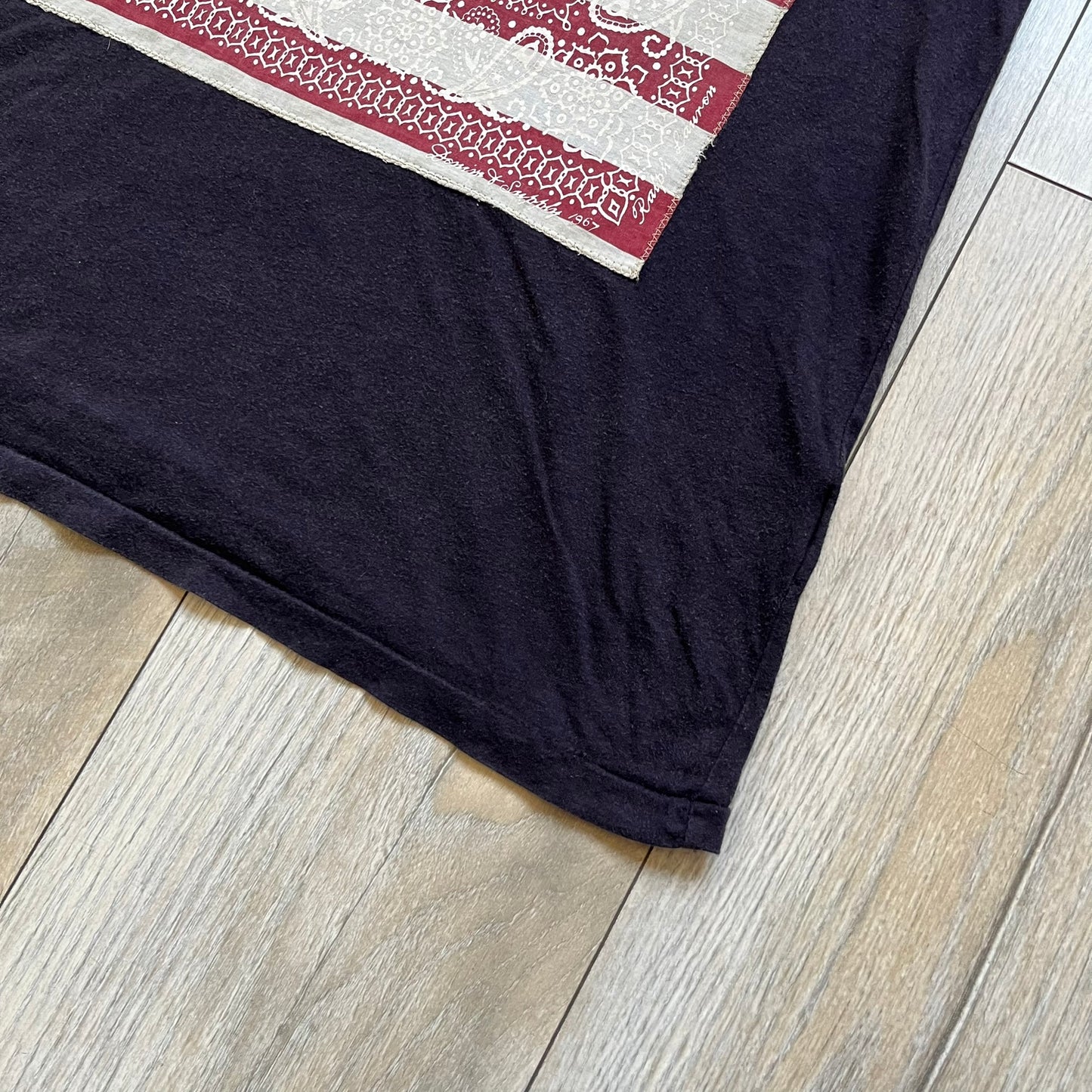 Ralph Lauren 2000s USA Bandana Flag Tee is a navy short-sleeve T-shirt made from 100% cotton. The front features a large USA flag constructed from fabric with a white bandana-style pattern, sewn onto the shirt for a raised effect. This piece comes from the Ralph Lauren Denim &amp; Supply line.