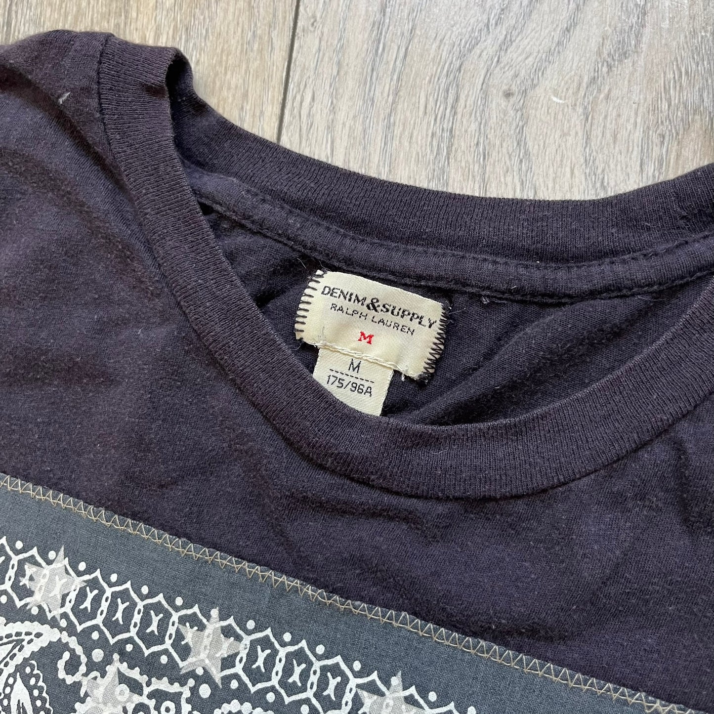 Ralph Lauren 2000s USA Bandana Flag Tee is a navy short-sleeve T-shirt made from 100% cotton. The front features a large USA flag constructed from fabric with a white bandana-style pattern, sewn onto the shirt for a raised effect. This piece comes from the Ralph Lauren Denim &amp; Supply line.