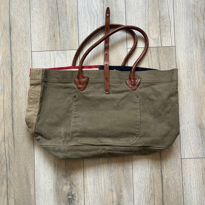 Ralph Lauren Denim &amp; Supply 1990s USA Flag Shoulder Bag is a large shoulder bag constructed from a mix of leather and cotton canvas. One side features a faded USA flag made from stitched canvas patches, while the reverse side is khaki canvas. The bag includes leather handles and a leather strap closure, an interior main compartment with additional smaller pockets, and a Denim &amp; Supply tag.
