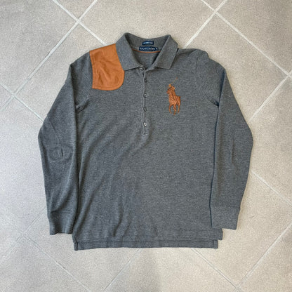 Ralph Lauren Leather Patch Gray Polo Longsleeve features a grey 100% cotton longsleeve polo with a brown leather patch on the right shoulder. The left chest has a raised 3D leather Polo logo, while the shirt has a button closure and is tagged “The Skinny Polo.”
