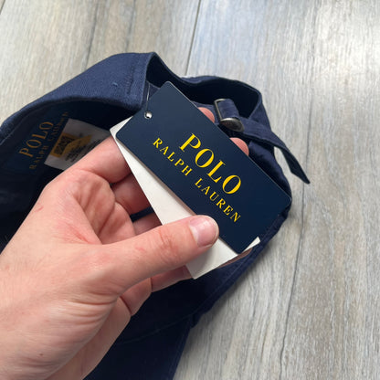 Ralph Lauren x Fortnite Navy Logo Baseball Cap is a navy cotton cap featuring bold embroidered branding on the front, including red Polo Ralph Lauren text and a Fortnite logo patch combined with a USA Ralph Lauren crest. The back includes a white embroidered Ralph Lauren logo and an adjustable strap for a custom fit.