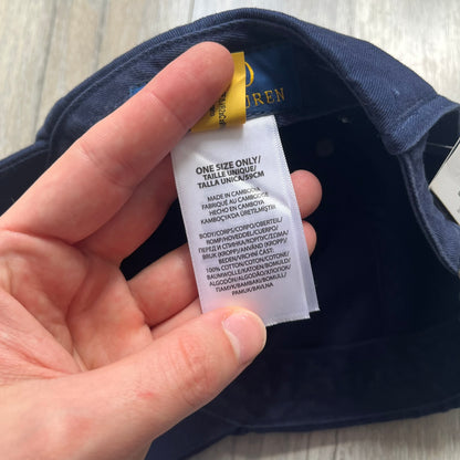 Ralph Lauren x Fortnite Navy Logo Baseball Cap is a navy cotton cap featuring bold embroidered branding on the front, including red Polo Ralph Lauren text and a Fortnite logo patch combined with a USA Ralph Lauren crest. The back includes a white embroidered Ralph Lauren logo and an adjustable strap for a custom fit.