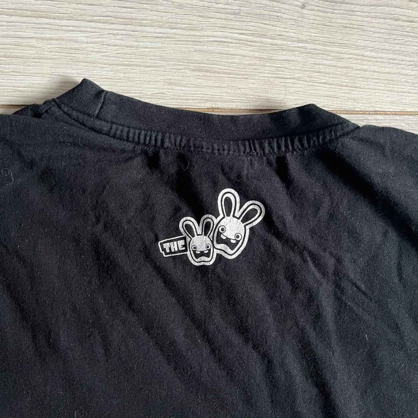 Raving Rabbids - known as “Lapins Crétins” in France - 2010 Tee in black, features a white Rabbid head inside a red circle with a slash, similar to a forbidden symbol. Officially licensed by Ubisoft, it comes with branding tags for collector and fan authenticity.&nbsp;