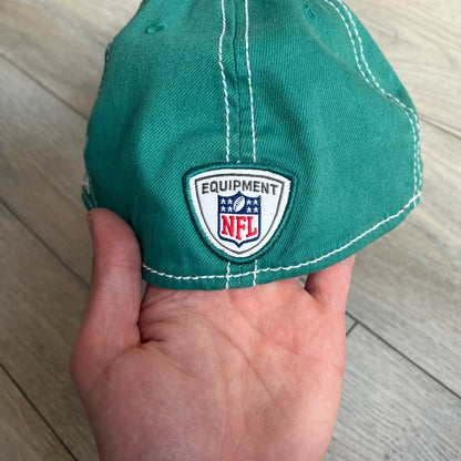 Reebok NFL Miami Dolphins Onfield Snapback Cap is a turquoise snapback featuring embroidered Miami Dolphins branding on the front, framed by two bold orange stripes positioned at the top and bottom of the front panel. The visor includes white stitching on the top surface and an orange underside for contrast. The side is detailed with a white Reebok logo, while the back features NFL Equipment and Onfield branding.