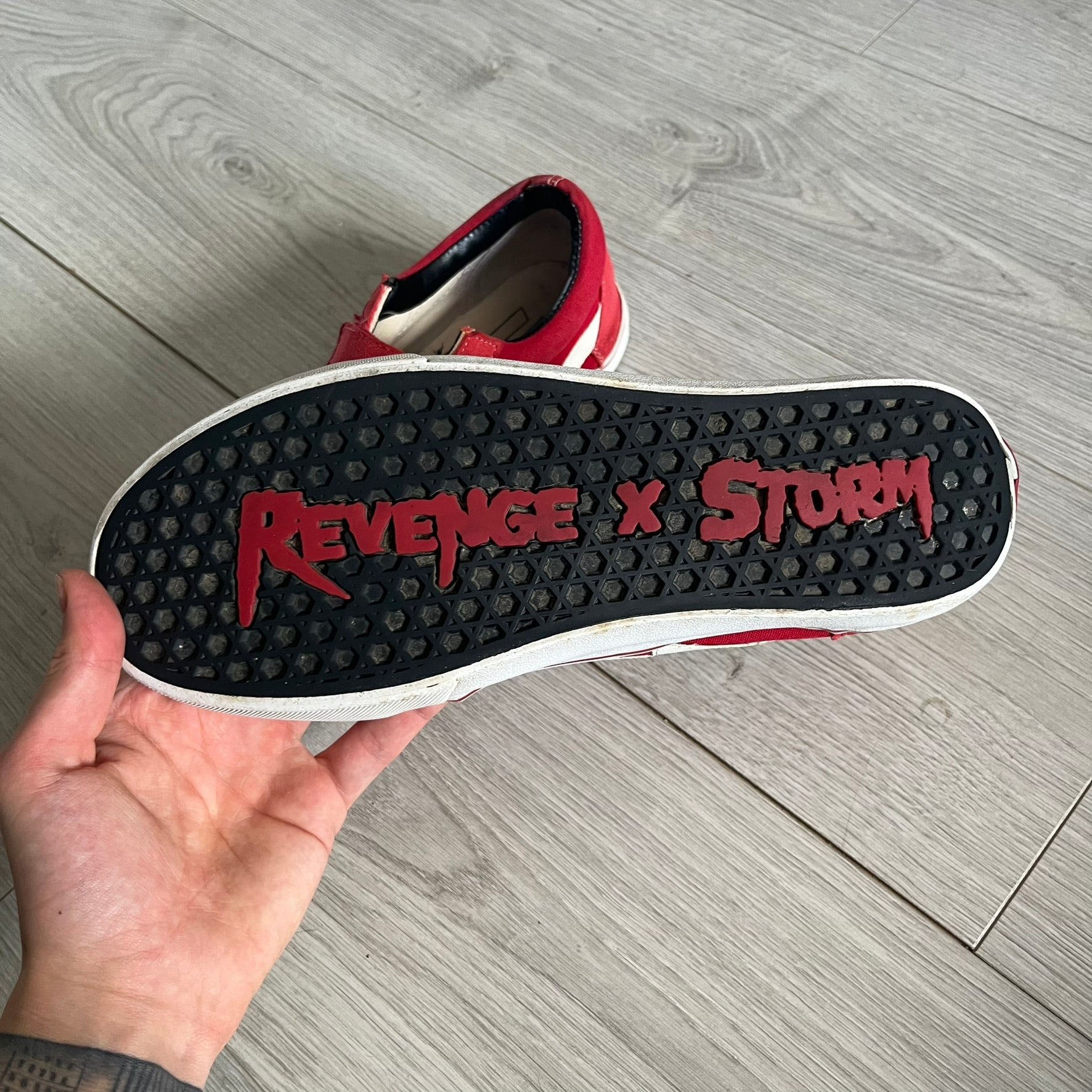 Revenge x Storm Red Strap Sneakers designed by Ian Connor. Featuring a red upper with white leather lightning bolts replacing the traditional Vans stripe. Finished with Velcro strap closures, white midsoles, black outsoles, and the signature “Revenge x Storm” branding in red on the sole.