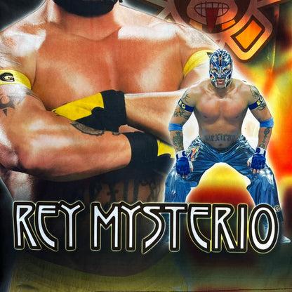 Rey Mysterio 2007 Kalciomania AOP Tee features an all-over print design with red, black, and white graphics throughout. The front includes a Rey Mysterio graphic with “Rey Mysterio” text, WWE logos, and additional printed details. The back features Rey Mysterio wearing a white mask with his signature and “619” graphic. The sleeves include a WWE logo and Rey Mysterio branding. Finished with a Kalciomania licensed tag.
