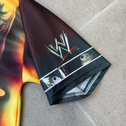 Rey Mysterio 2007 Kalciomania AOP Tee features an all-over print design with red, black, and white graphics throughout. The front includes a Rey Mysterio graphic with “Rey Mysterio” text, WWE logos, and additional printed details. The back features Rey Mysterio wearing a white mask with his signature and “619” graphic. The sleeves include a WWE logo and Rey Mysterio branding. Finished with a Kalciomania licensed tag.
