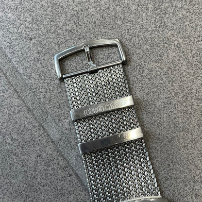 Roberto Cavalli 2000's Ellisse Analog Watch features a curved silver-tone case with a textured mesh bracelet and adjustable strap. The dial has a pearlescent finish that changes slightly depending on the angle, with no hour numbers and a small Roberto Cavalli logo at the bottom.
