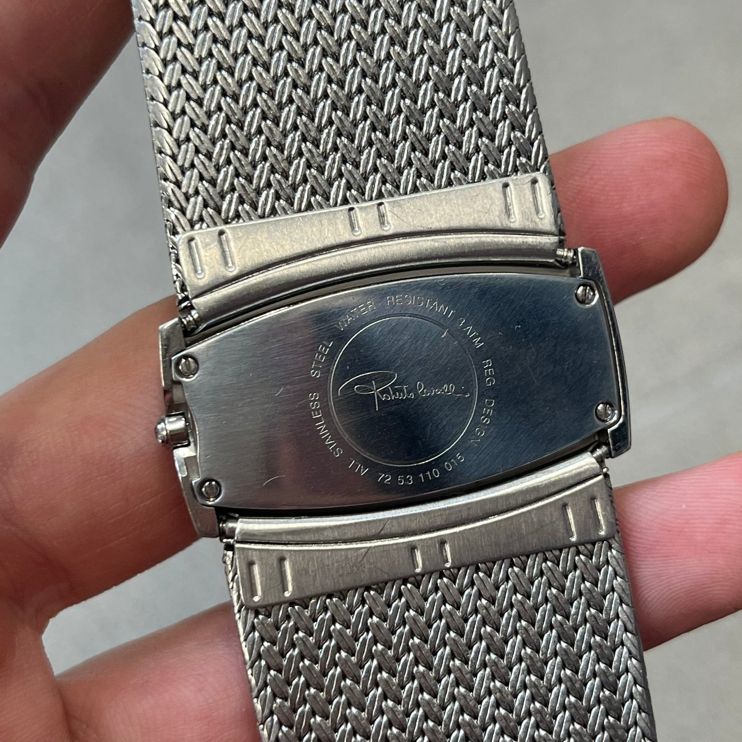 Roberto Cavalli 2000's Ellisse Analog Watch features a curved silver-tone case with a textured mesh bracelet and adjustable strap. The dial has a pearlescent finish that changes slightly depending on the angle, with no hour numbers and a small Roberto Cavalli logo at the bottom.
