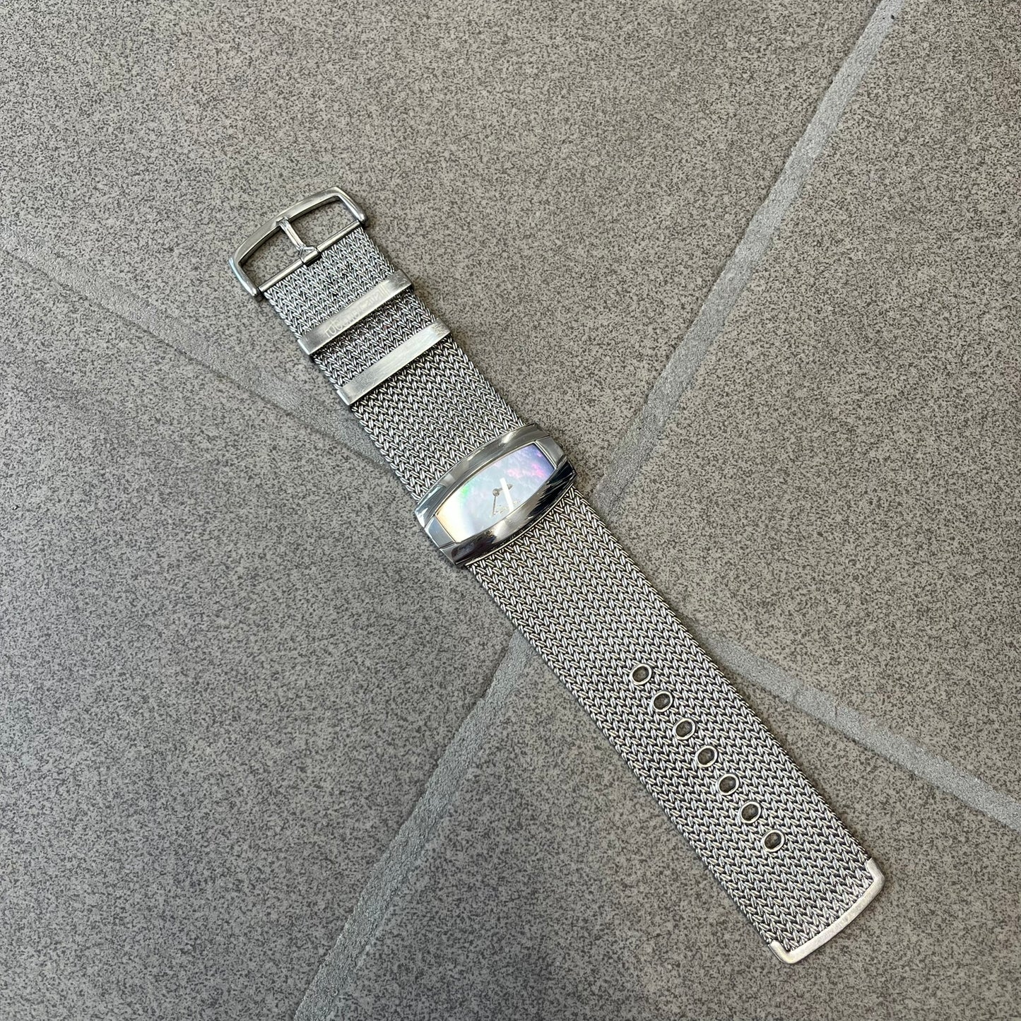 Roberto Cavalli 2000's Ellisse Analog Watch features a curved silver-tone case with a textured mesh bracelet and adjustable strap. The dial has a pearlescent finish that changes slightly depending on the angle, with no hour numbers and a small Roberto Cavalli logo at the bottom.
