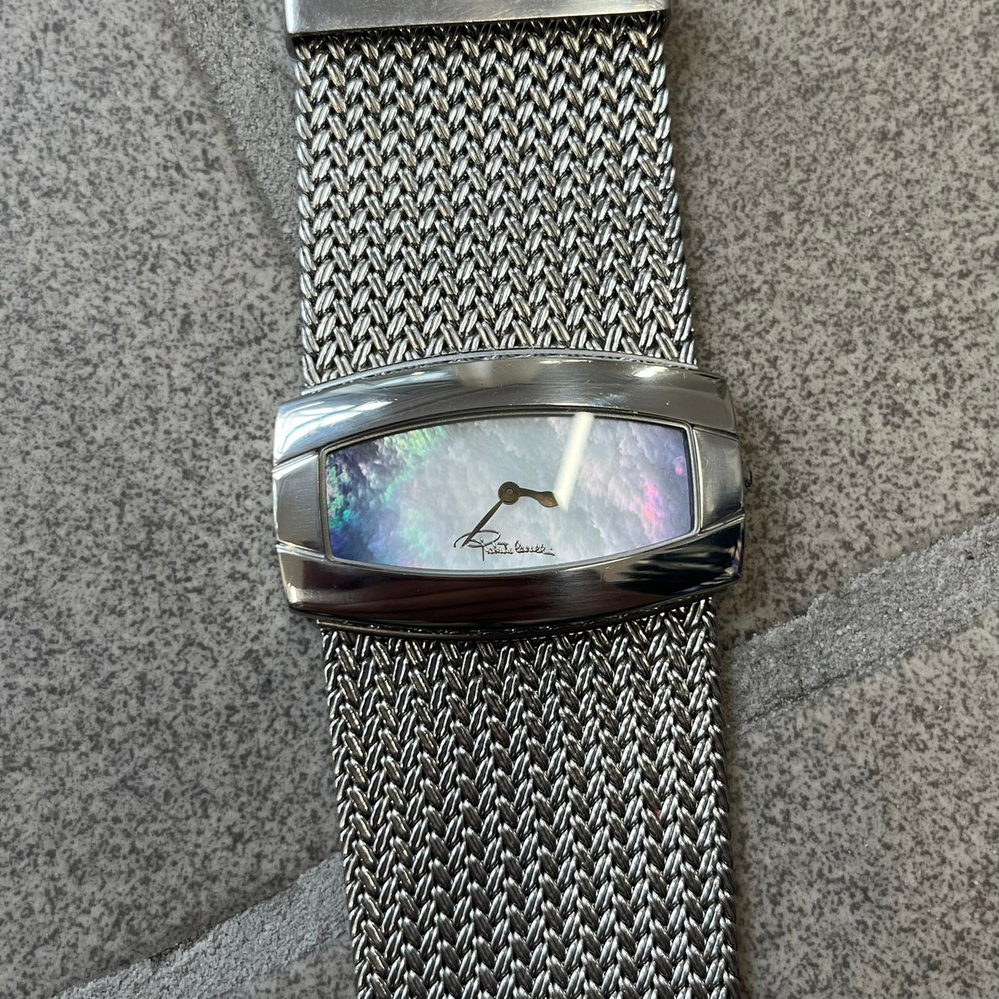 Roberto Cavalli 2000's Ellisse Analog Watch features a curved silver-tone case with a textured mesh bracelet and adjustable strap. The dial has a pearlescent finish that changes slightly depending on the angle, with no hour numbers and a small Roberto Cavalli logo at the bottom.
