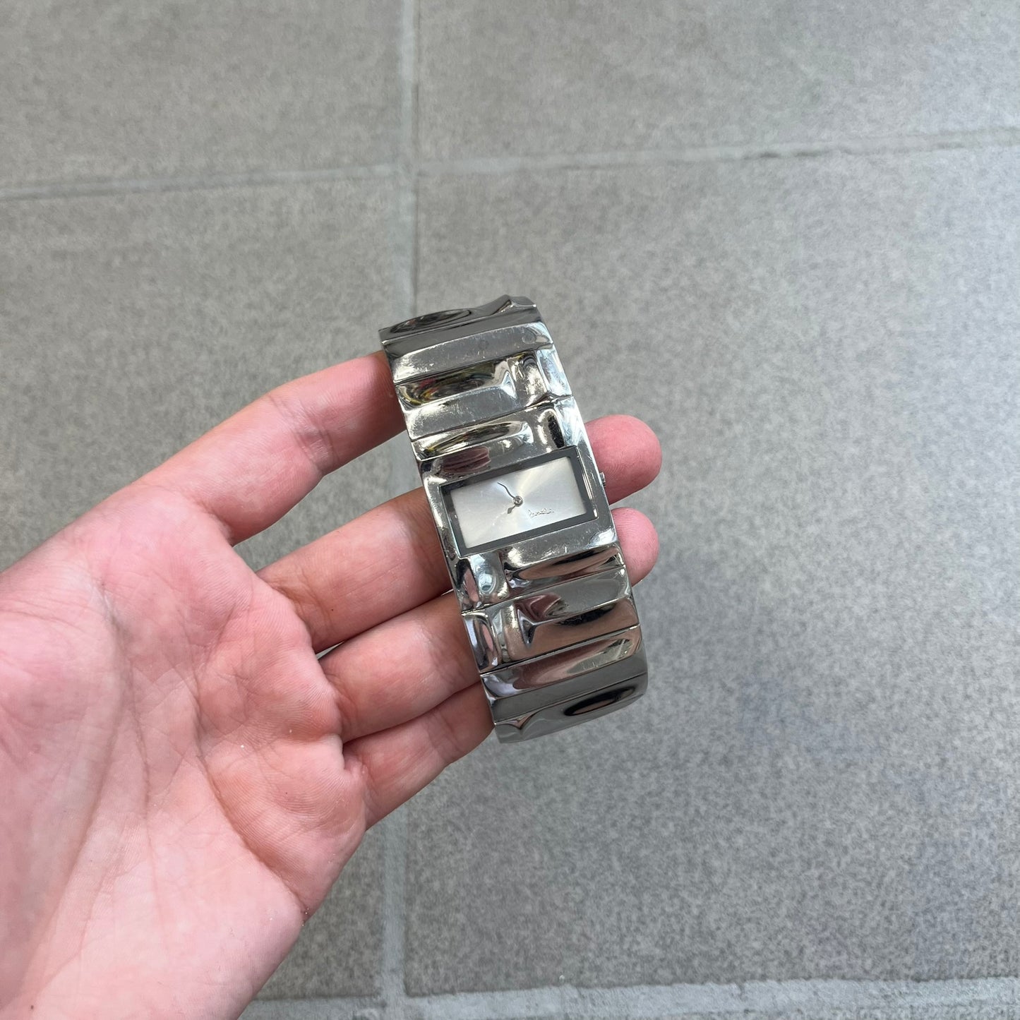  Roberto Cavalli 2000s Silver Croco Analog Watch features a sleek stainless steel design with a case that matches the width of the bracelet for a seamless look. The bracelet is made from silver-tone square links with irregular raised crocodile-inspired texture details. The minimalist white dial has no hour numerals, only the Roberto Cavalli branding.