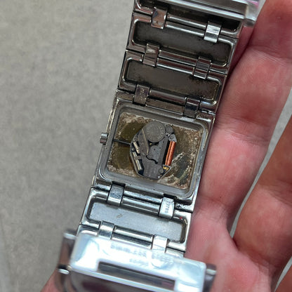  Roberto Cavalli 2000s Silver Croco Analog Watch features a sleek stainless steel design with a case that matches the width of the bracelet for a seamless look. The bracelet is made from silver-tone square links with irregular raised crocodile-inspired texture details. The minimalist white dial has no hour numerals, only the Roberto Cavalli branding.