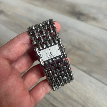 Roberto Cavalli Bones Steel Oryza Analog Watch R7253124015 is a stainless steel analog watch featuring a silver-tone case and integrated bracelet designed with bone-shaped link elements. The dial is aligned with the width of the bracelet, creating a continuous one-piece construction, and includes Cavalli-designed hands. This model uses a quartz movement.