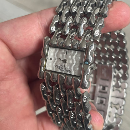 Roberto Cavalli Bones Steel Oryza Analog Watch R7253124015 is a stainless steel analog watch featuring a silver-tone case and integrated bracelet designed with bone-shaped link elements. The dial is aligned with the width of the bracelet, creating a continuous one-piece construction, and includes Cavalli-designed hands. This model uses a quartz movement.