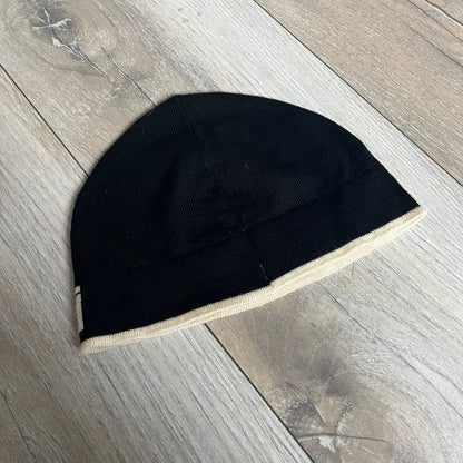 Roberto Cavalli Gold Logo Beanie is a black knit beanie made in Italy from 100% wool. The front features a raised gold Cavalli emblem, with “Roberto Cavalli” text in white integrated into the knit on both sides of the logo. The beanie has a thin wool construction suitable for lightweight wear.