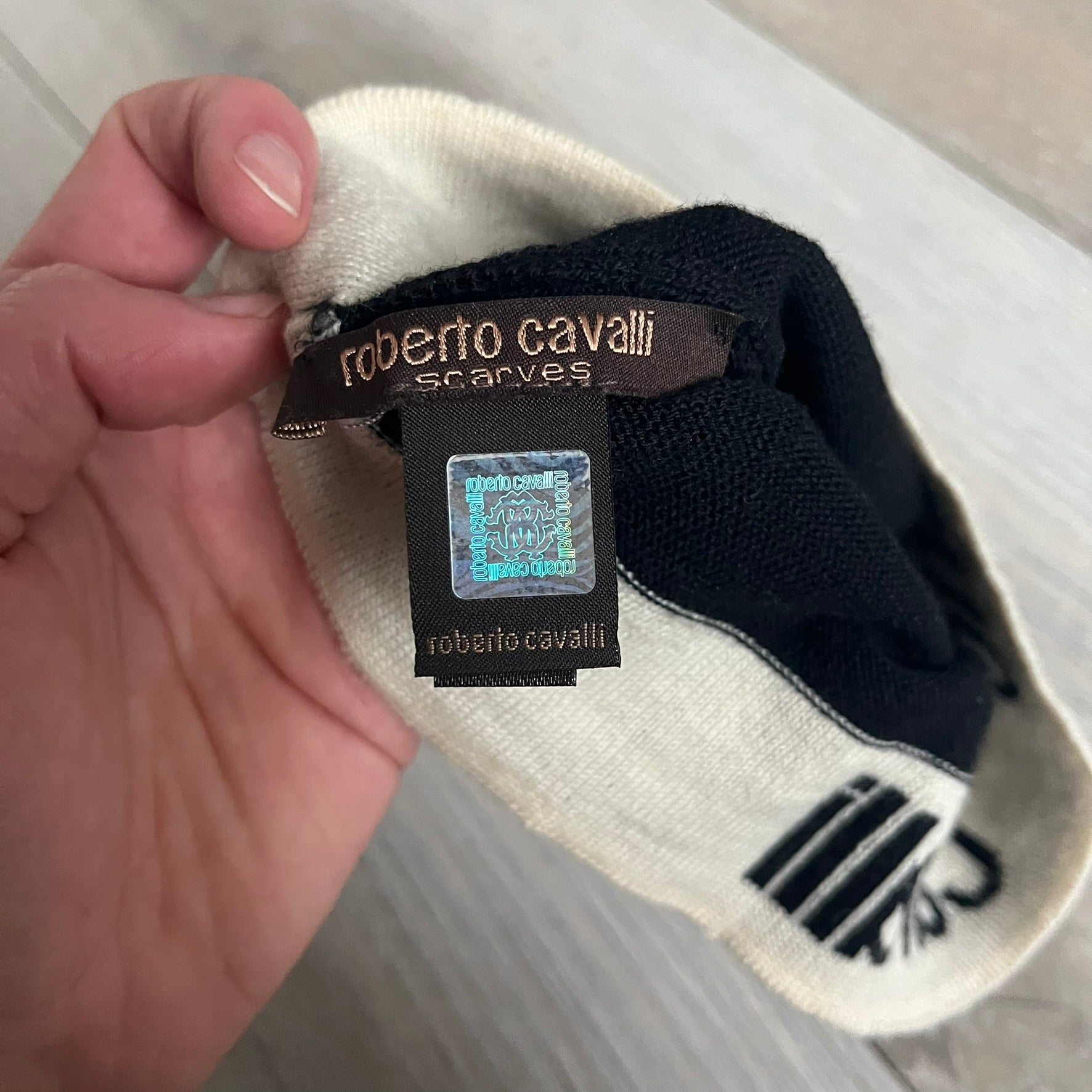 Roberto Cavalli Gold Logo Beanie is a black knit beanie made in Italy from 100% wool. The front features a raised gold Cavalli emblem, with “Roberto Cavalli” text in white integrated into the knit on both sides of the logo. The beanie has a thin wool construction suitable for lightweight wear.