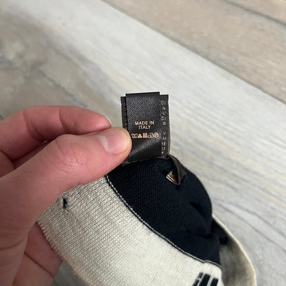 Roberto Cavalli Gold Logo Beanie is a black knit beanie made in Italy from 100% wool. The front features a raised gold Cavalli emblem, with “Roberto Cavalli” text in white integrated into the knit on both sides of the logo. The beanie has a thin wool construction suitable for lightweight wear.