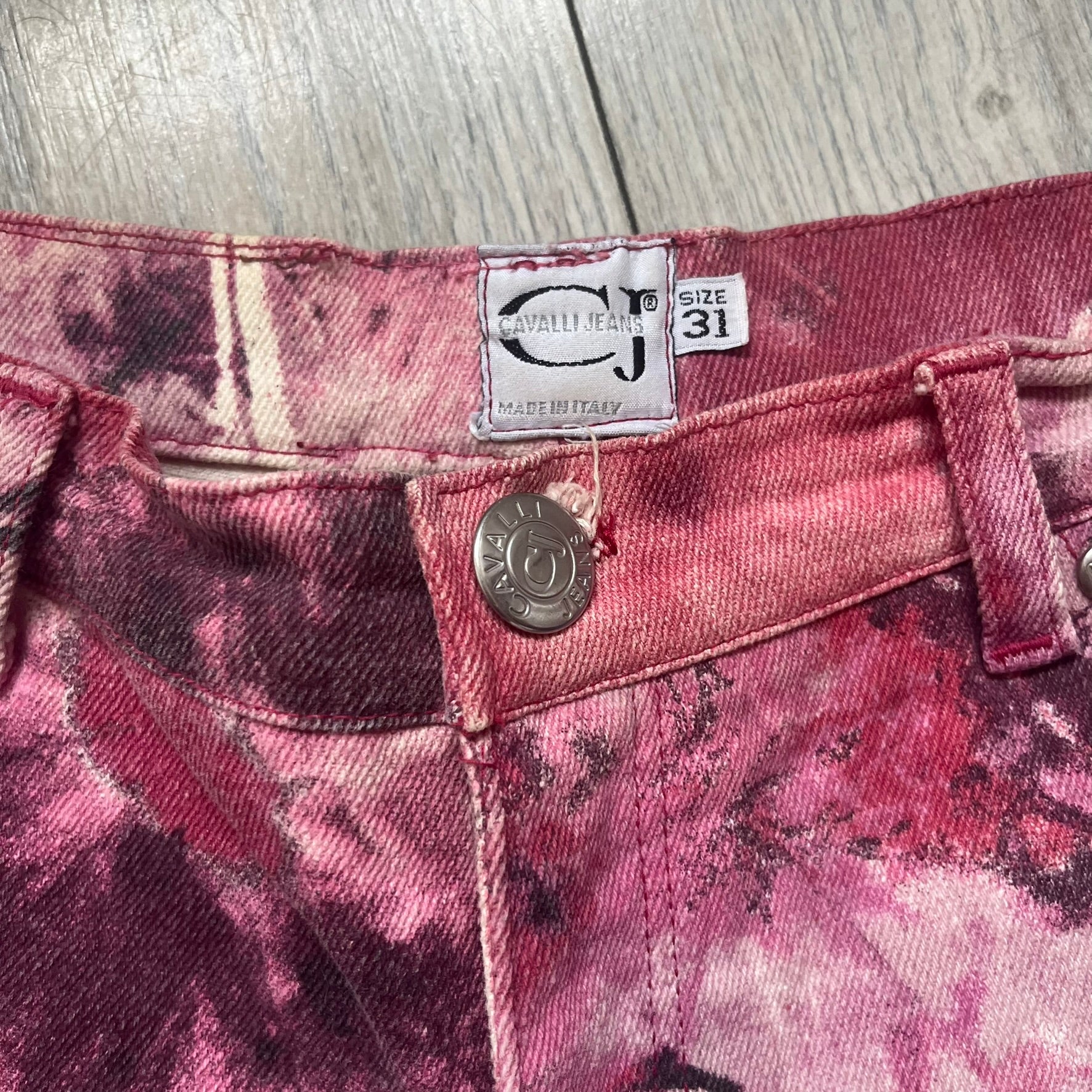 Roberto Cavalli Pink Floral 2000’s Jeans are made in Italy from 98% cotton and 2% elastane. The jeans feature an all-over floral print in multiple shades of pink, ranging from light to dark, with a hand-painted effect across the fabric. Details include branded buttons, a leather logo tab at the back, and classic five-pocket construction with two front and two back pockets.
