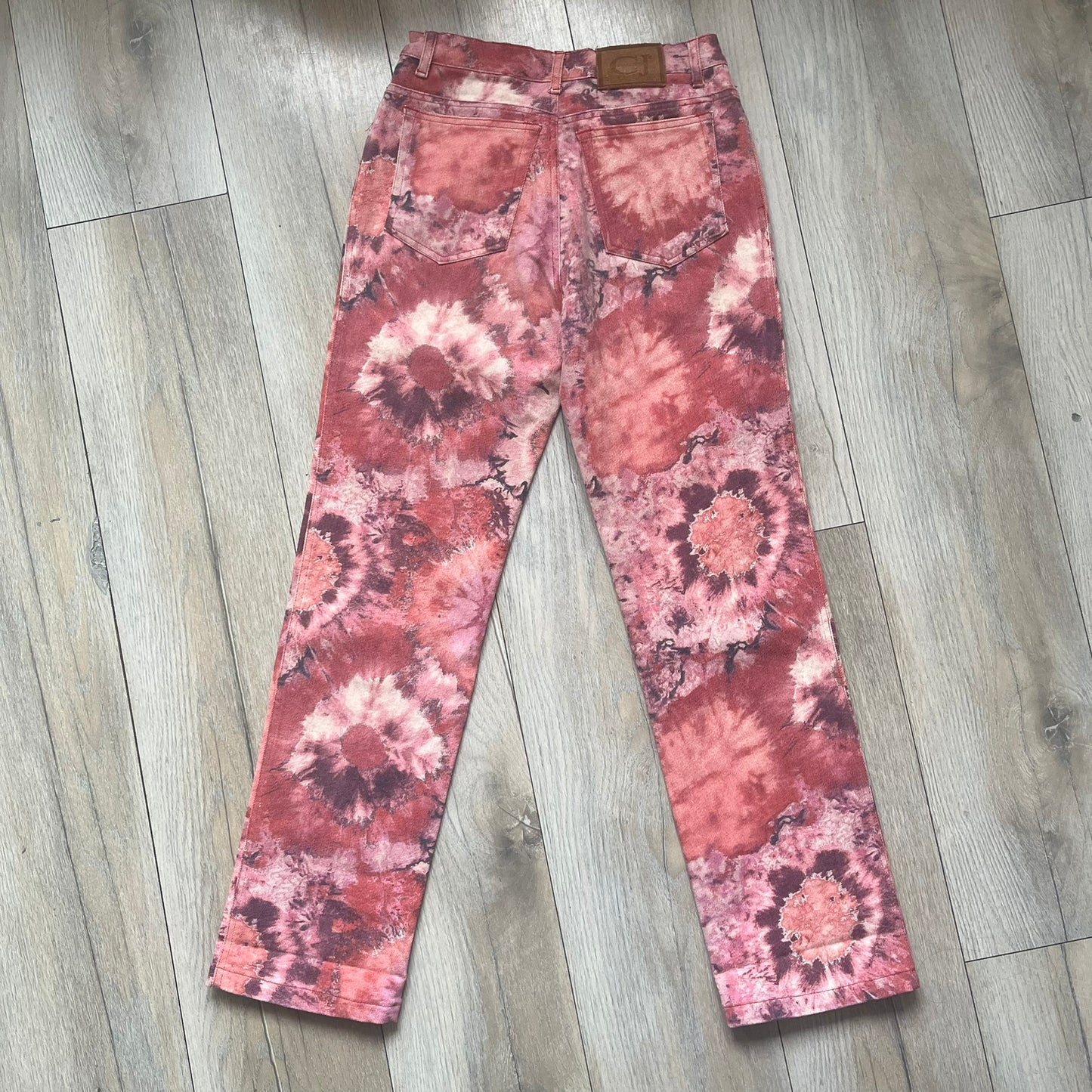 Roberto Cavalli Pink Floral 2000’s Jeans are made in Italy from 98% cotton and 2% elastane. The jeans feature an all-over floral print in multiple shades of pink, ranging from light to dark, with a hand-painted effect across the fabric. Details include branded buttons, a leather logo tab at the back, and classic five-pocket construction with two front and two back pockets.