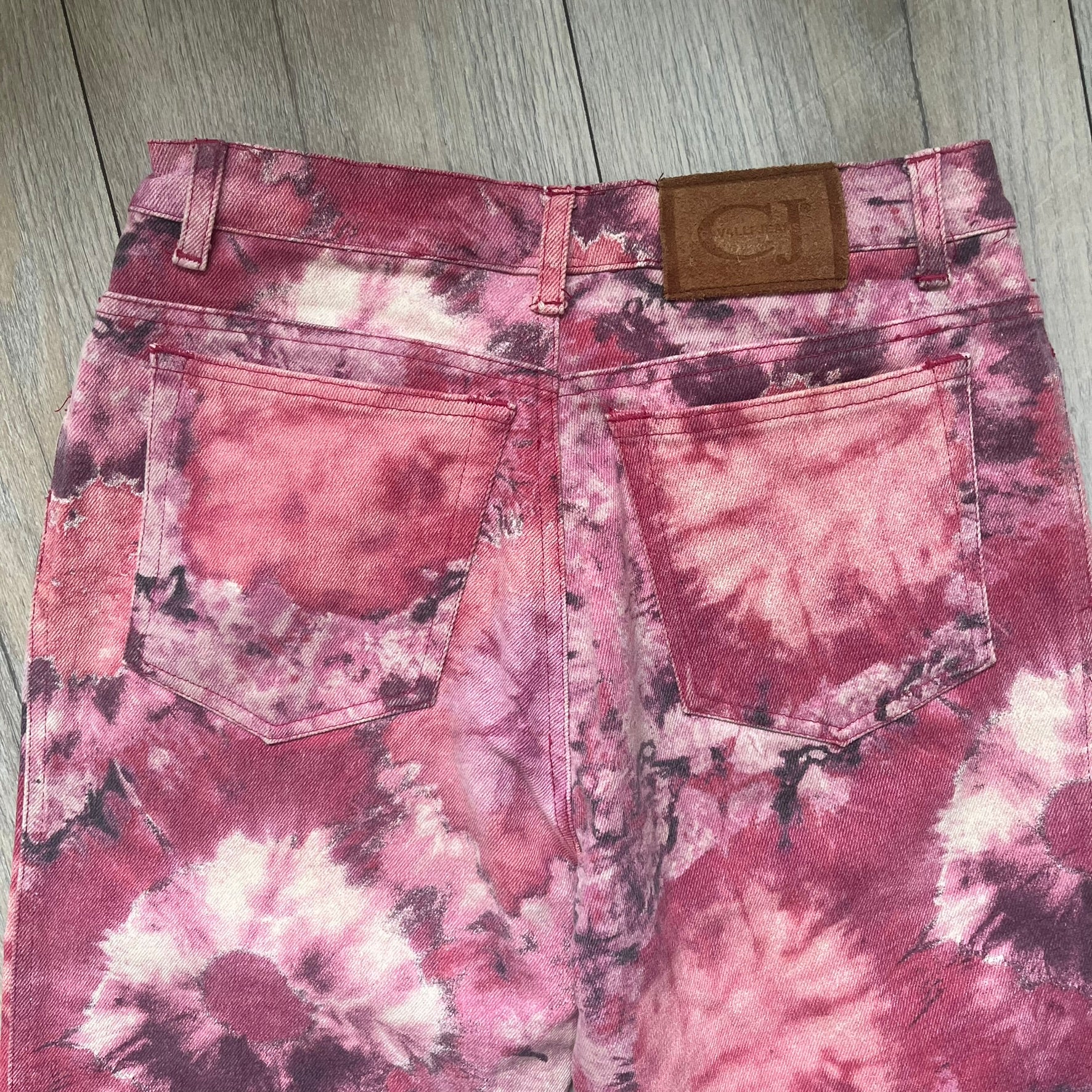 Roberto Cavalli Pink Floral 2000’s Jeans are made in Italy from 98% cotton and 2% elastane. The jeans feature an all-over floral print in multiple shades of pink, ranging from light to dark, with a hand-painted effect across the fabric. Details include branded buttons, a leather logo tab at the back, and classic five-pocket construction with two front and two back pockets.
