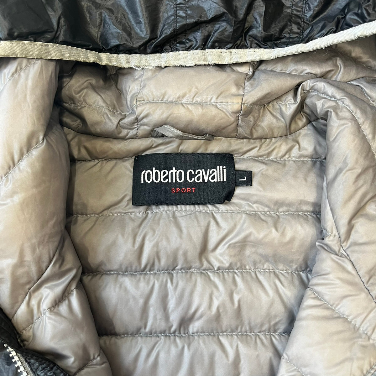 Roberto Cavalli Sport 2010's Black Lightweight Jacket is a lightweight hooded jacket in black with a gray interior, featuring two front pockets and star logo zipper pulls. A rubber Roberto Cavalli Sport logo patch sits on the chest, with a smaller matching patch on the upper back.