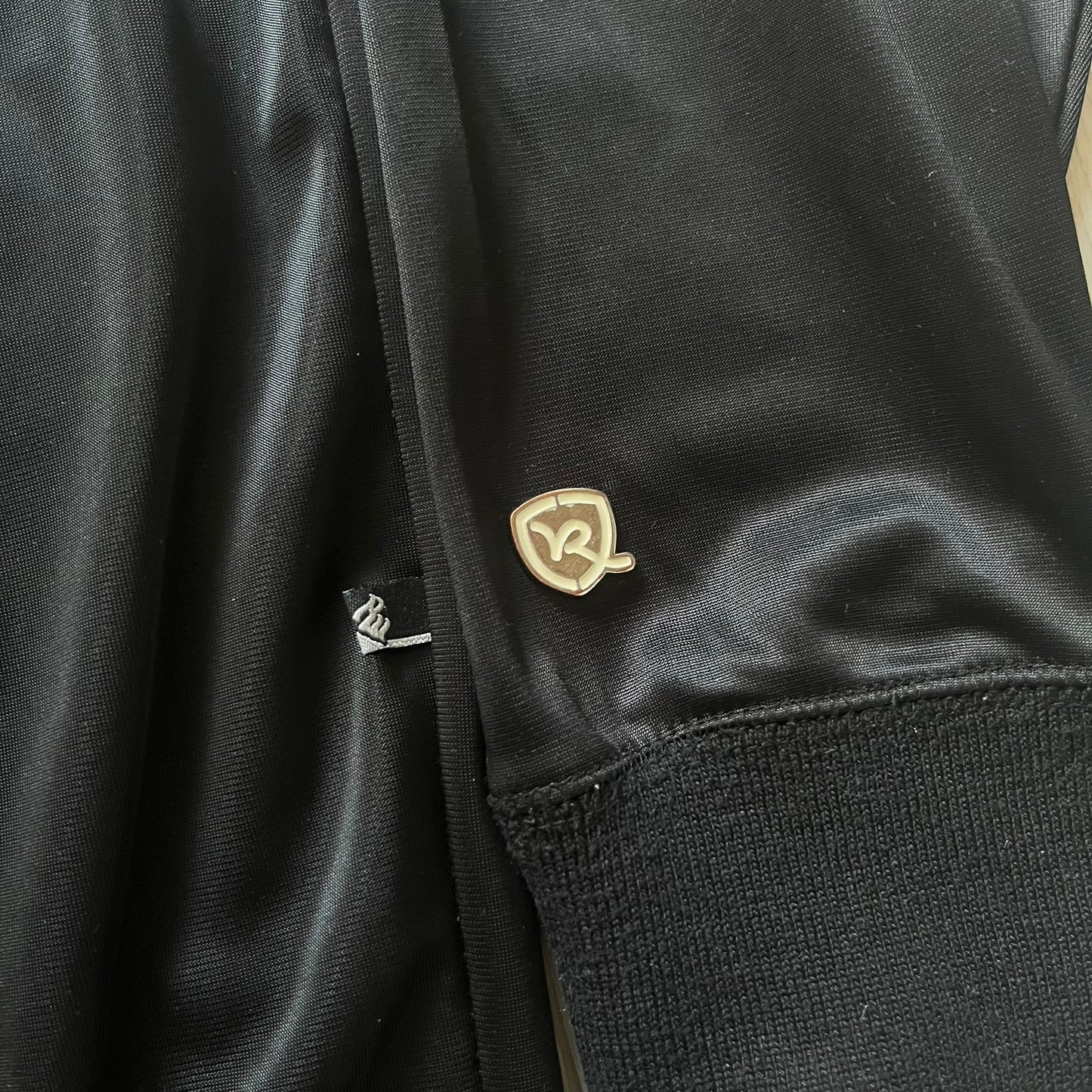 Vintage Rocawear black track jacket featuring a small embroidered chest logo and big white branding across the back. Silver zipper and wrist emblem add refined details to this early-2000s streetwear classic.