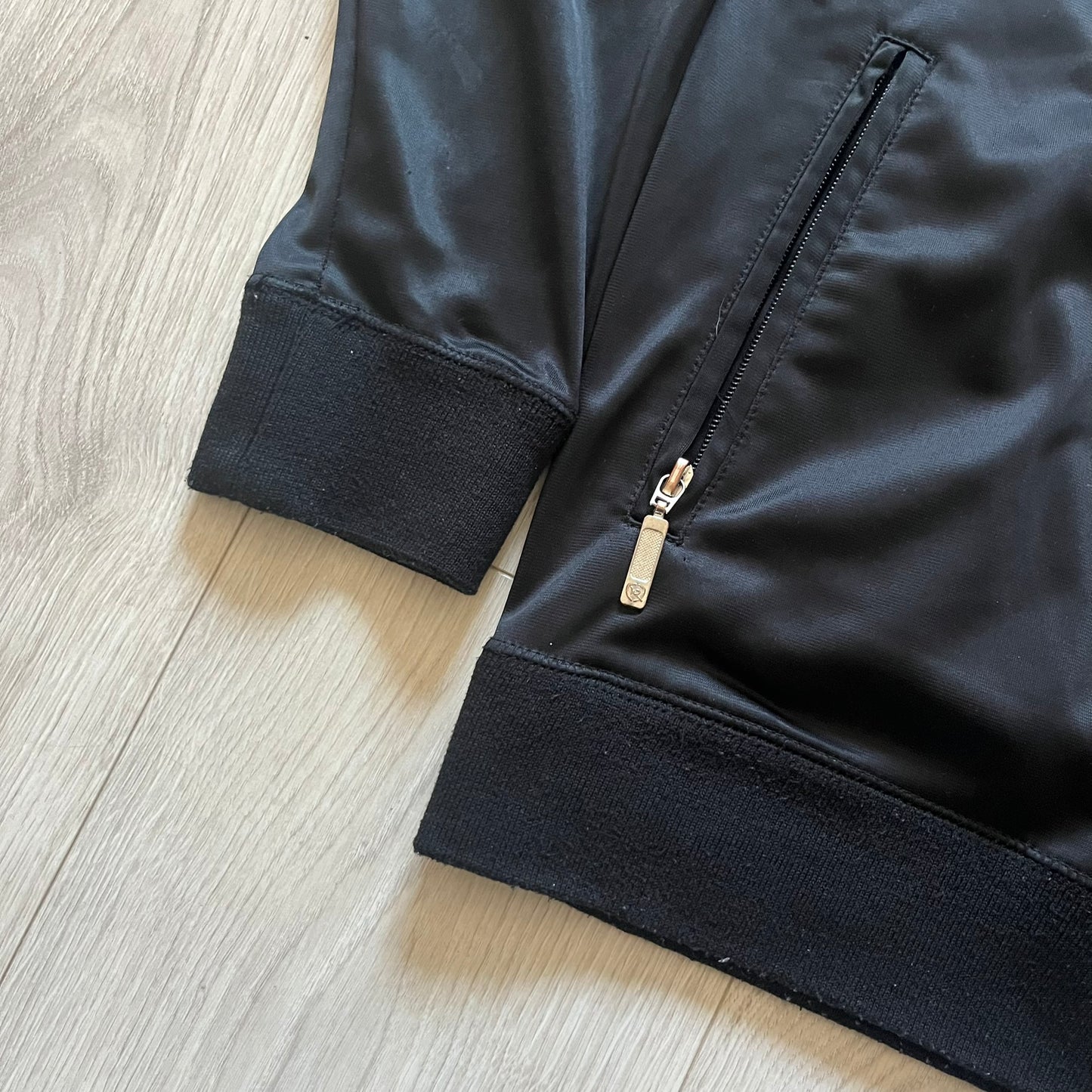 Vintage Rocawear black track jacket featuring a small embroidered chest logo and big white branding across the back. Silver zipper and wrist emblem add refined details to this early-2000s streetwear classic.