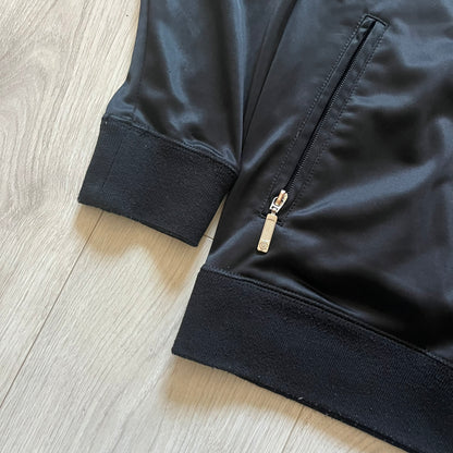 Vintage Rocawear black track jacket featuring a small embroidered chest logo and big white branding across the back. Silver zipper and wrist emblem add refined details to this early-2000s streetwear classic.