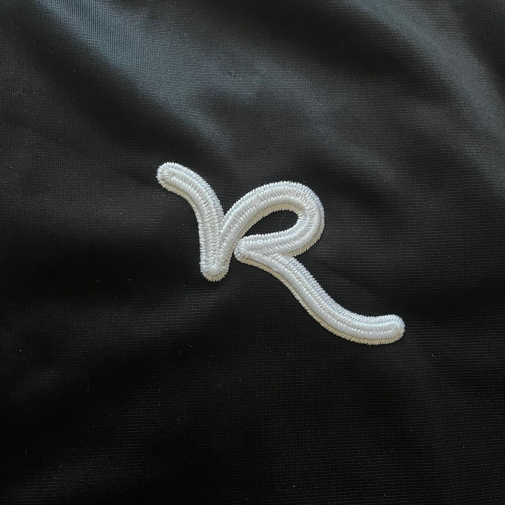 Vintage Rocawear black track jacket featuring a small embroidered chest logo and big white branding across the back. Silver zipper and wrist emblem add refined details to this early-2000s streetwear classic.